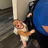 toddler, child, indoor, floor, wooden_floor, chair, person, blue_shirt, wall, curious, holding, standing, casual, expression, home, young_child, socks, light, hair, diaper