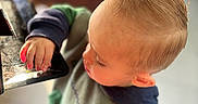Joshua joined the competition — help win amazing prizes! toddler, child, curious, indoor, natural_light, blond_hair, long_eyelashes, green_clothing, hoodie, hand, face, exploring, black_surface, floor, candid, portrait, soft_light, young_child, casual_clothing, closeup