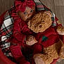 baby, child, teddy_bear, red_clothing, bow, plush_toy, cushioned_chair, wooden_floor, indoor, portrait, cute, smiling, person, infant, holiday_theme, cozy, soft_toy, fashion, sitting, warm_colors