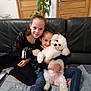 child, dog, indoor, smiling, couch, hugging, pet, white_dog, casual_clothing, plant, wooden_door, family, happy, leather_couch, home, sitting, portrait, two_children, cozy, friendly