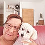 woman, dog, glasses, red_couch, living_room, bookshelf, book, white_dog, portrait, indoor, smile, face, hand, wooden_door, cactus, decor, fan, casual, cozy, home