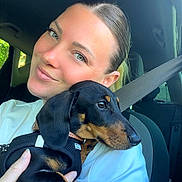 Archie participe au concours pour gagner de l'argent avec cette photo : woman, dog, puppy, dachshund, car, seatbelt, white_shirt, smile, portrait, indoor, pet, holding, black_dog, tan_markings, human_hand, short_hair, seat, window, daylight, closeup