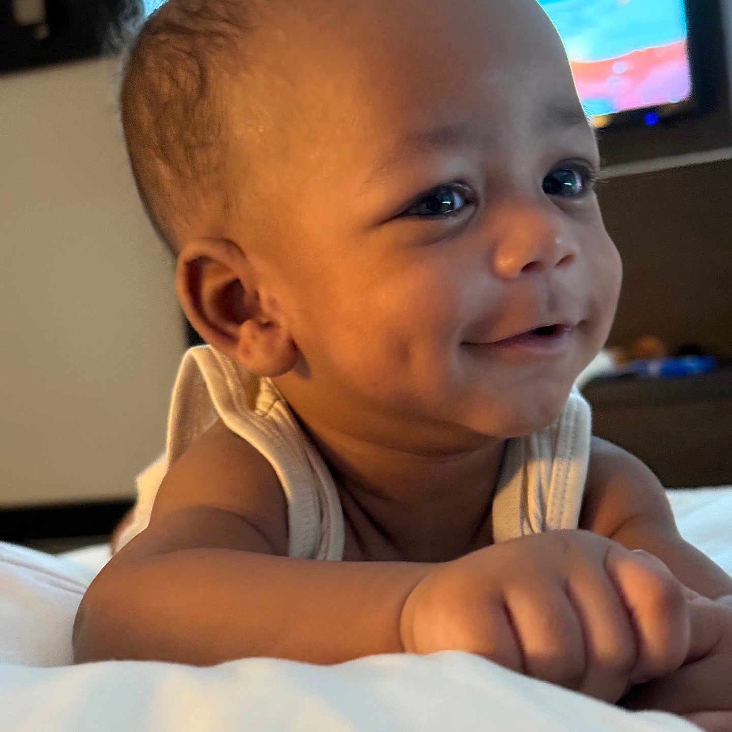 Nasir Cayden joined the competition — help win amazing prizes! arm, baby, background, bed, child, closeup, cute, dimples, face, hand, happy, indoors, infant, person, portrait, skin, smiling, soft_lighting, television, white_bedspread