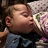 baby, sleeping, infant, portrait, face, closed_eyes, indoors, blanket, pillow, bed, cozy, peaceful, dark_lighting, close_up, hair, blue_clothing, floral_pattern, home, resting, child