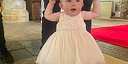 Lillian is registered to the contest to win money with this photo: adult_hands, baby, black_pants, blue_shirt, carpet, casual_shoes, child, church, cute, dress, floor, helping, indoor, person, pink_shoes, socks, stone_wall, support, toddler, walking