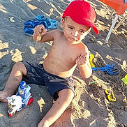 Anas a rejoint le concours — aidez-le/la à gagner de superbes lots ! child, toddler, beach, sand, toy, red_cap, shorts, barefoot, sunlight, shadow, chair, towel, sand_toys, playing, summer, outdoor, vacation, footwear, plastic_toy, relaxation