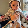 Ozzy is registered to the contest to win money with this photo: baby, child, hoodie, tongue_out, tattoo, hand, watch, shoes, checkered, person, indoors, blurred_background, table, clothing, cute, expression, holding, infant, face, smile