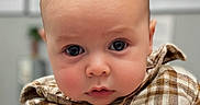 Ozzy is registered to the contest to win money with this photo: baby, child, face, portrait, close_up, plaid_shirt, clothing, infant, cute, eyes, expression, soft_light, indoors, young_child, head, skin, person, newborn, looking, apparel