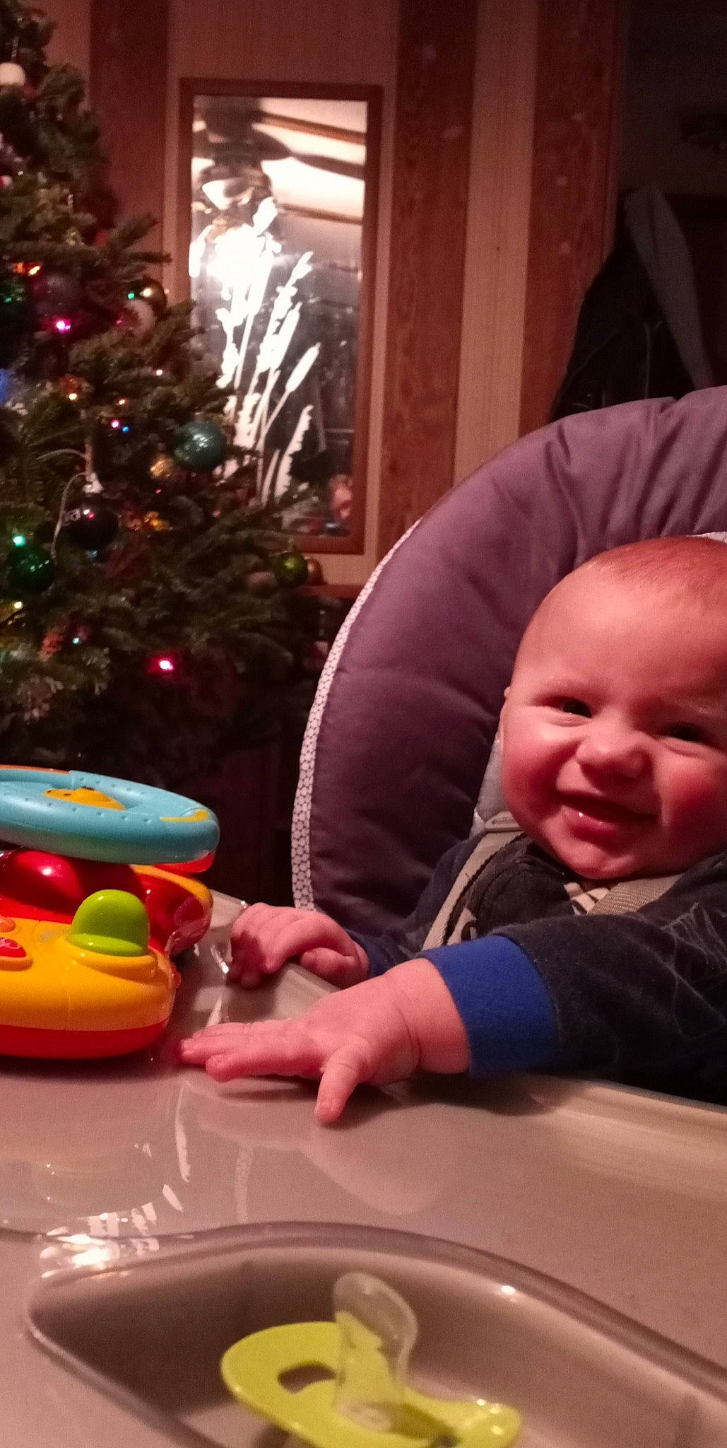 Xavyer is registered to the contest to win money with this photo: baby, baby_toddler_clothing, child, christmas_ornament, christmas_tree, comfort, event, fun, head, holiday, holiday_ornament, ornament, person, plant, room, sitting, smile, table, toddler, toy