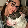 woman, dog, glasses, earbuds, couch, indoor, snuggling, closeup, pet, face, portrait, comfort, affection, casual, brown_hair, white_dog, gray_dog, expression, nose_ring, relaxation