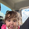 car, child, clothing, clouds, cute, daylight, expression, face, hair, head, indoors, person, pink_shirt, playful, seat, seatbelt, sky, toddler, tongue_out, window