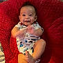 baby, infant, smiling, clapping, cushion, red, onesie, patterned_clothing, foot, happy, indoor, child, cute, face, person, baby_girl, baby_boy, playful, soft, texture