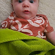 Zoie joined the competition — help win amazing prizes! baby, infant, child, blanket, green_blanket, orange_shirt, patterned_clothing, wide_eyes, face, head, lying_down, soft_surface, expression, indoor, person, cute, young_child, skin, portrait, comfort