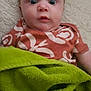 baby, infant, child, blanket, green_blanket, orange_shirt, patterned_clothing, wide_eyes, face, head, lying_down, soft_surface, expression, indoor, person, cute, young_child, skin, portrait, comfort