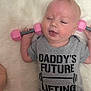 Harper joined the competition — help win amazing prizes! baby, infant, cute, pink_dumbbells, gray_shirt, text_on_shirt, lying_down, fluffy_surface, smiling, child, young, person, playful, indoor, exercise, fitness, small_weights, casual_clothing, happy, adorable