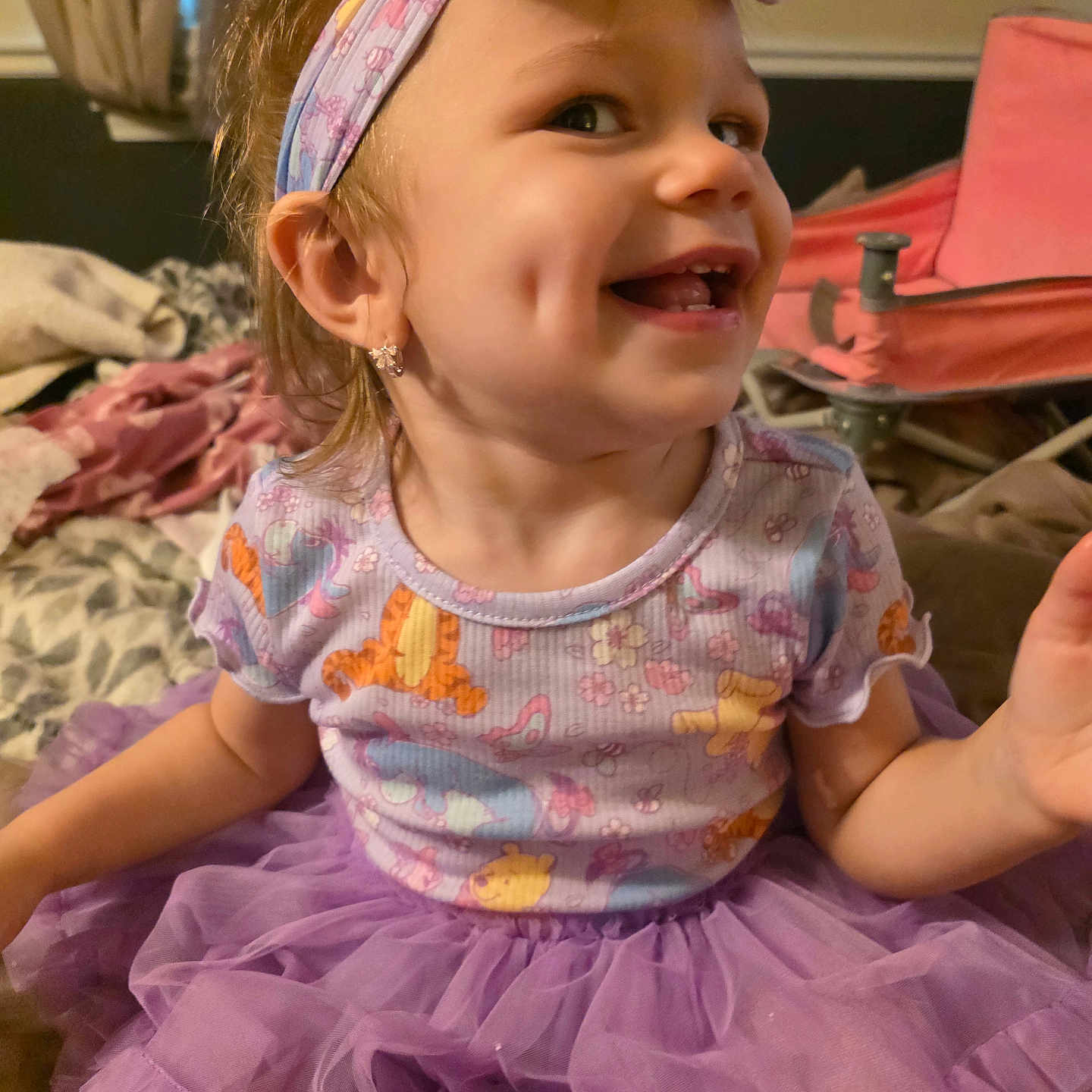 Genesis is registered to the contest to win money with this photo: toddler, child, smile, dimples, headband, earrings, purple_tutu, cartoon_clothing, indoor, curtains, bed, blanket, furniture, happy, portrait, cute, person, clothing, young_child, playful