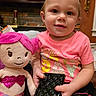 toddler, child, plush_toy, mermaid_doll, pink_hair, glitter, wallet, indoor, brick_wall, earrings, short_hair, pink_shirt, black_skirt, toy, person, cute, smile, sitting, holding, cozy