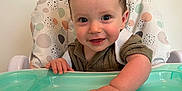 Freddie is registered to the contest to win money with this photo: baby, child, clothing, cute, decor, expression, face, feeding, furniture, hand, happy, highchair, home, indoor, person, portrait, seat, smiling, table, young_child