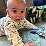 baby, crawling, dinosaur_print, blanket, hand, face, smile, indoor, plush_toy, cozy, child, cute, pattern, clothing, infant, expression, person, home, soft_focus, curious