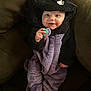 baby, child, costume, fuzzy_clothing, hood, purple, black, smiling, toy, ring, couch, indoor, cute, infant, face, hand, foot, seated, cozy, happy