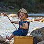 toddler, child, river, water, rocks, fishing, stick, hat, overalls, yellow_boots, outdoor, nature, summer, sunlight, wooden_box, barefoot, portrait, playful, candid, adventure