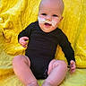 baby, infant, child, smiling, portrait, sitting, yellow_blanket, black_onesie, medical_tube, feeding_tube, face, eyes, mouth, bald, indoor, close_up, happy, legs, feet, photography