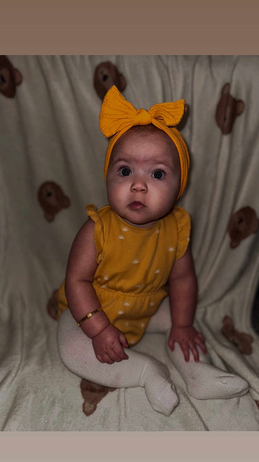 Alayah-Ray is registered to the contest to win money with this photo: baby, child, yellow_outfit, headband, bracelet, blanket, teddy_bear_pattern, sitting, curious, indoors, cute, portrait, infant, white_tights, soft_lighting, closeup, small_hands, chubby_cheeks, expression, person