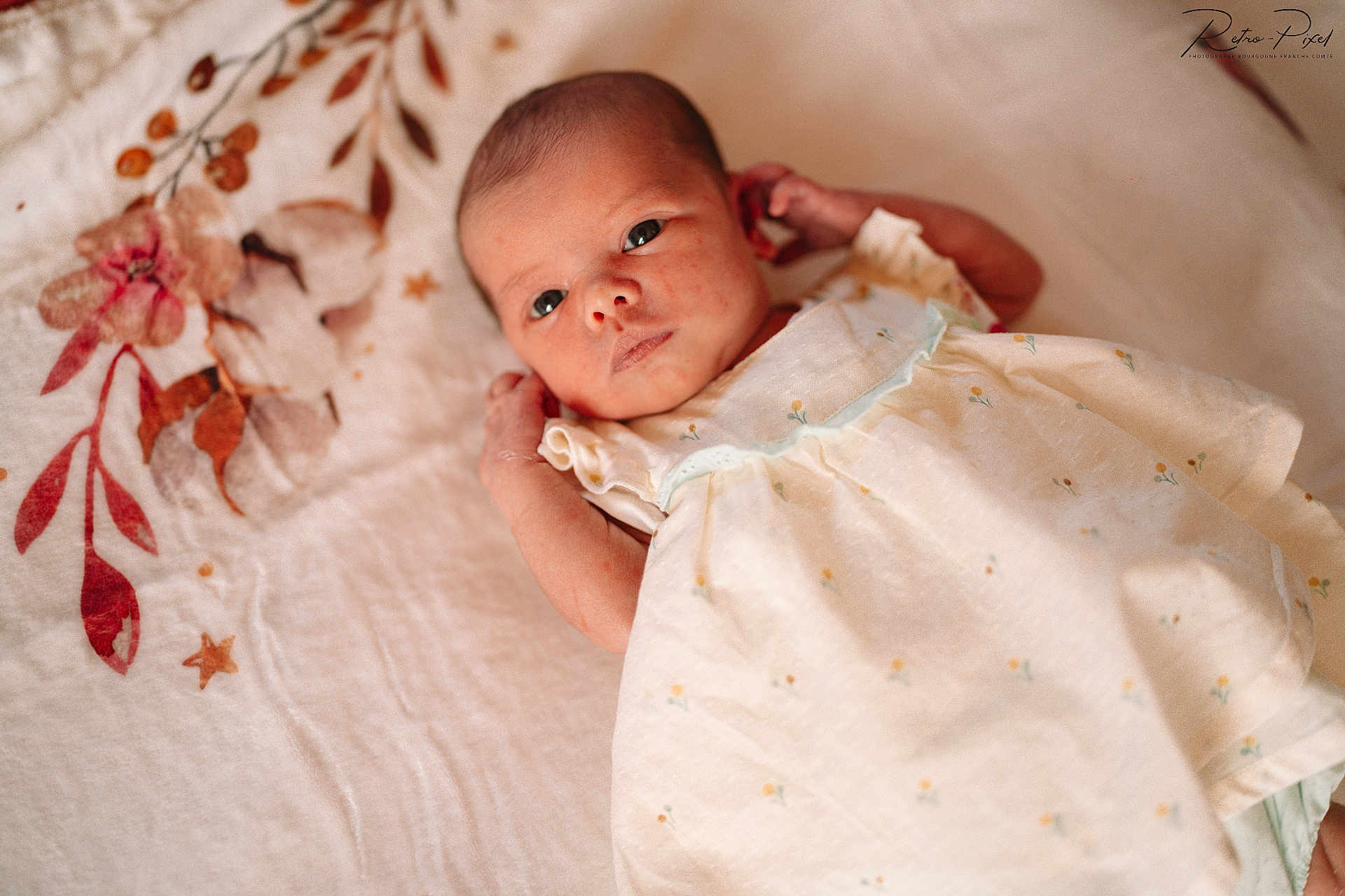 émy participe au concours pour gagner de l'argent avec cette photo : baby, newborn, infant, dress, blanket, floral_pattern, face, eyes, skin, lying_down, soft_texture, cute, small, child, portrait, indoors, peaceful, calm, clothing, sleepwear