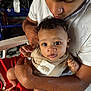 Isaiah is registered to the contest to win money with this photo: baby, child, person, young_adult, curly_hair, indoor, affection, holding, clothing, face, arm, red_shorts, white_shirt, closeup, portrait, skin, seated, looking, expression, love