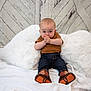 baby, child, infant, blue_eyes, brown_shirt, jeans, boots, white_pillows, fluffy, white_sheet, wooden_wall, rustic, sitting, hands_clasped, curious, indoor, portrait, cute, young, playful