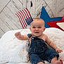 baby, child, denim_overalls, flag, american_flag, smiling, cute, indoor, cushion, white_fur, blue_eyes, patriotic, red_star, blue_star, wooden_background, happy, sitting, infant, portrait, celebration