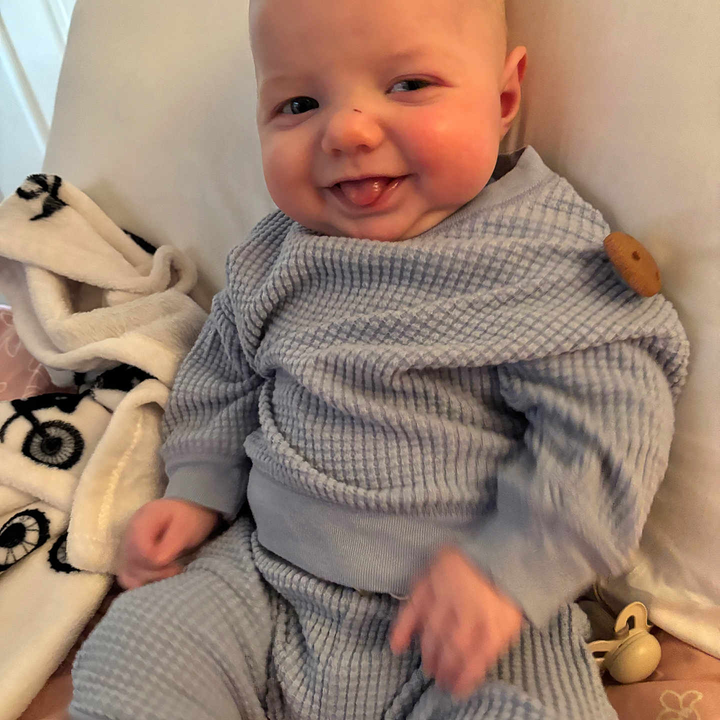 Rowin joined the competition — help win amazing prizes! baby, bedding, blanket, blue_outfit, chubby_cheeks, closeup, cushion, cute, hands, happy, indoor, infant, pacifier, portrait, sitting, smile, soft_texture, tongue_out, waffle_knit, wooden_toy