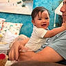 adult, arms, baby, blue_wall, child, cozy, cushion, family, furniture, happy, holding, indoors, infant, nursery, parent, photography, portrait, smiling, soft_toys, white_clothing