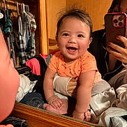 Liam joined the competition — help win amazing prizes! baby, child, infant, smiling, laughing, mirror, reflection, portrait, indoor, bedroom, wardrobe, clothing, hanger, orange_shirt, shorts, sitting, hand, phone, photographer, happy