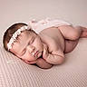 newborn, baby, sleeping, infant, portrait, headband, floral_headband, blanket, knitted_blanket, pink, peaceful, curled_up, lying_down, indoors, soft_lighting, photography, closeup, face, bare_skin, relaxed