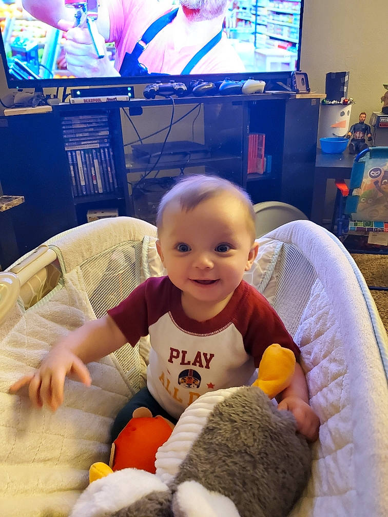 Roman is registered to the contest to win money with this photo: baby, blue, chair, child, comfort, couch, desk, electronic_device, flooring, fun, furniture, happy, joy, leisure, living_room, person, skin, smile, t_shirt, table