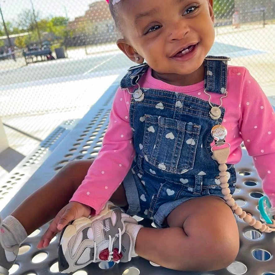 Callie is registered to the contest to win money with this photo: accessories, baby, bodypart, clothing, coat, face, happy, head, jacket, outdoors, pants, person, photography, playarea, portrait, shorts, sitting, smile, summer, sunglasses