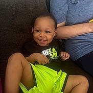 Jamari Holmes joined the competition — help win amazing prizes! toddler, child, smiling, couch, neon_shorts, black_shirt, pen, happy, indoor, person, seated, relaxed, casual_clothing, shorts, bright_colors, face, cute, young_child, home, family