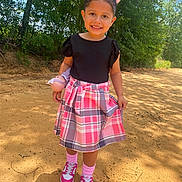 Skylar is registered to the contest to win money with this photo: child, girl, smiling, outdoor, doll, pink_bows, plaid_skirt, black_top, pink_sneakers, socks, dirt_path, trees, sunlight, nature, happy, person, cute, playful, summer, fashion