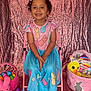 Skylar joined the competition — help win amazing prizes! child, smiling, dress, pink_chair, easter_eggs, plush_toy, headband, curly_hair, pink_background, colorful_clothing, sandals, toy_basket, holiday, celebration, happy, indoors, portrait, festive, easter_basket, cute