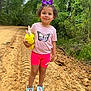 child, girl, outdoor, dirt_path, greenery, stuffed_animal, yellow_bunny, purple_bow, pink_shorts, butterfly_tshirt, frozen_shoes, smiling, curly_hair, nature, trees, casual_clothing, footwear, summer, playful, walking