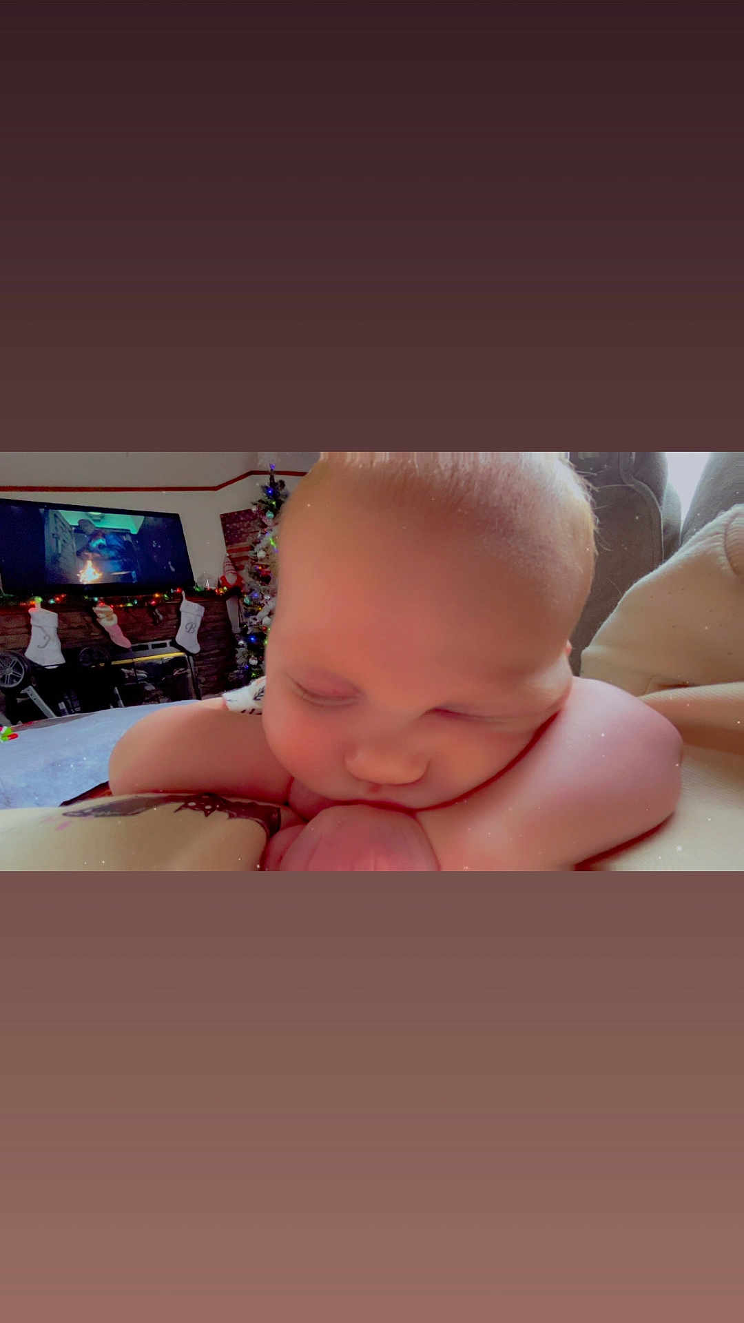 Danielle is registered to the contest to win money with this photo: baby, sleeping, face, arm, christmas_tree, stockings, television, holiday, indoor, cozy, child, resting, blanket, couch, furniture, person, home, decor, relaxing, cute