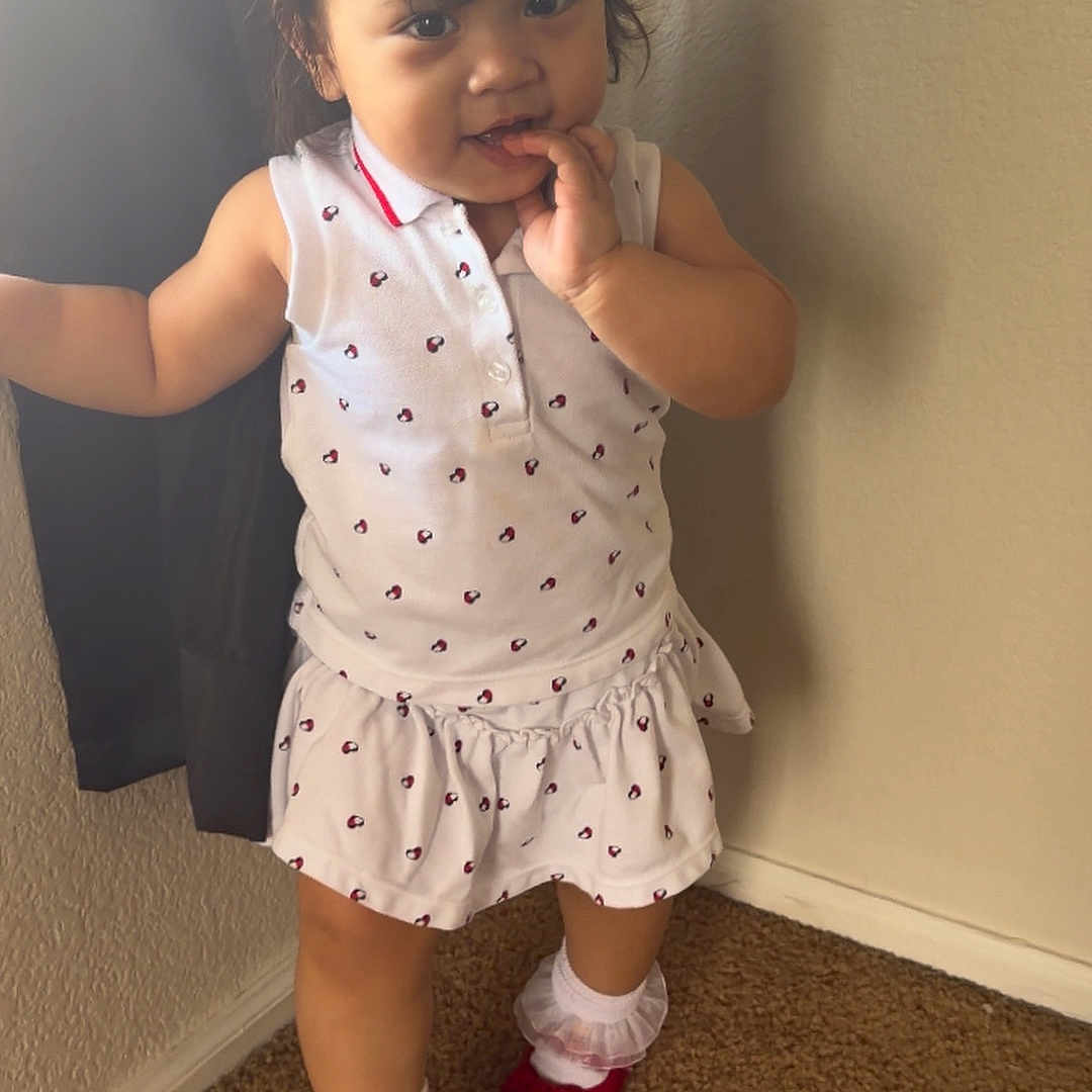 Kristabelle is registered to the contest to win money with this photo: toddler, child, girl, white_dress, red_shoes, socks, carpet, indoor, curtain, wall, standing, playing, cute, young_child, portrait, person, smiling, hair_ties, light, shadow