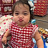 toddler, child, shopping_cart, red_dress, checkered_pattern, hair_bow, grocery_store, pouting, cute, baby, face, person, clothing, retail, supermarket, packaging, sitting, funny_expression, indoor, hand