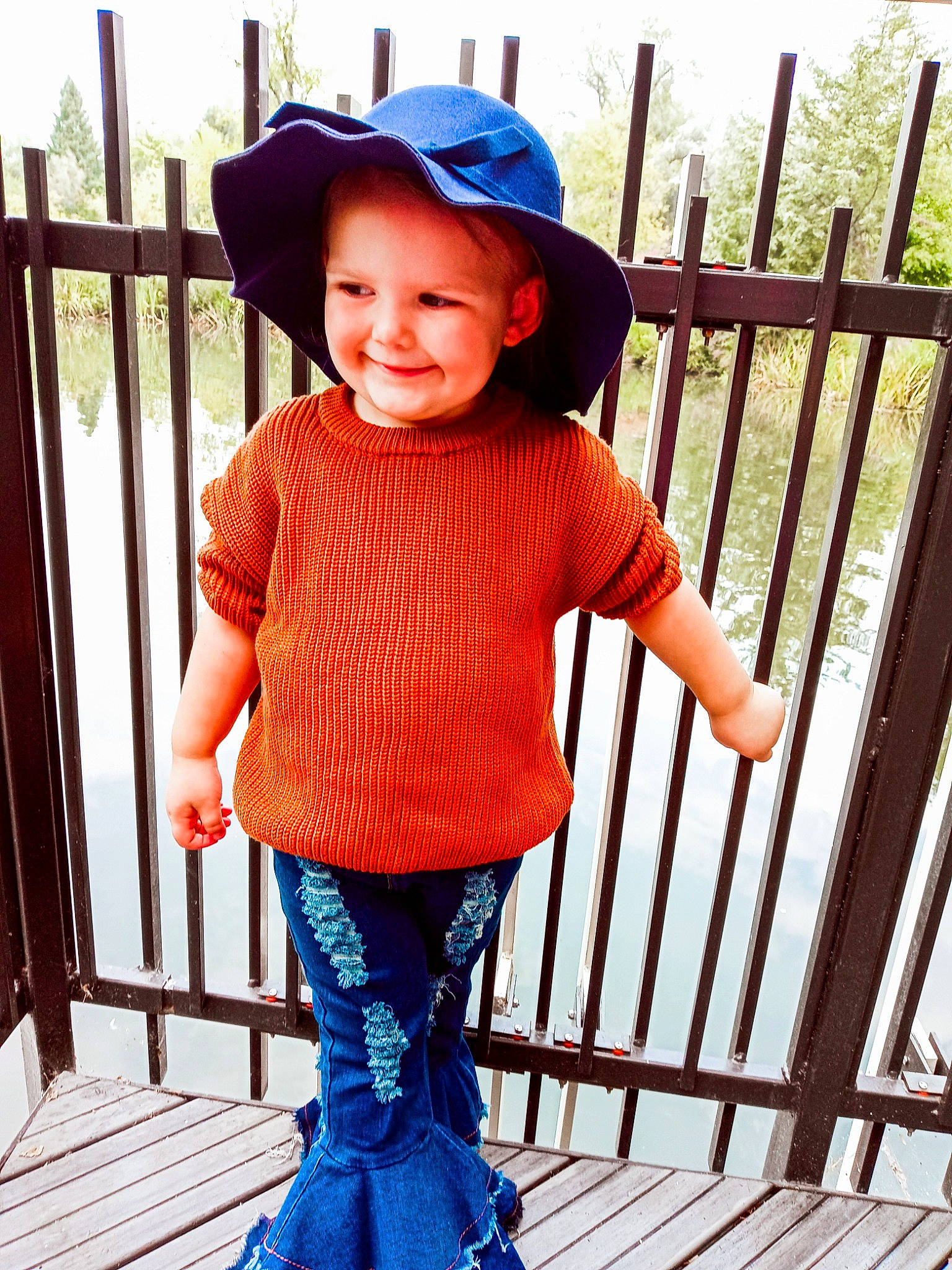 Kenleigh joined the competition — help win amazing prizes! baby_toddler_clothing, blue, cap, cool, fence, happy, hat, headwear, joy, neck, outerwear, person, photograph, product, sleeve, smile, standing, street_fashion, sun_hat, textile