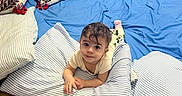 Adnan is registered to the contest to win money with this photo: baby, child, infant, portrait, smiling, lying_down, pillow, cushion, bed, blanket, blue, white, indoors, living_room, furniture, home, wood_floor, cozy, playful, photography