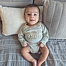Adnan is registered to the contest to win money with this photo: baby, child, infant, smiling, portrait, sitting, sofa, couch, cushions, indoor, home, clothing, onesie, text_on_clothing, patterned_fabric, cross_legged, happy, face, family, photography