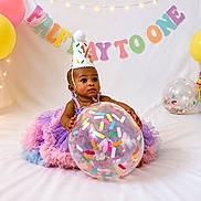 Nevaeh is registered to the contest to win money with this photo: baby, birthday, half_birthday, balloon, confetti, tutu, party_hat, celebration, colorful, pastel_colors, smiling, child, decorations, banner, festive, cute, indoor, sitting, happy, photography