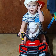 Jaxx joined the competition — help win amazing prizes! child, toddler, cap, toy_vehicle, honda, puppy, dog, indoor, floor, wooden_door, smiling, blue_eyes, striped_shirt, shorts, handlebars, pet, cute, playtime, baby, fun