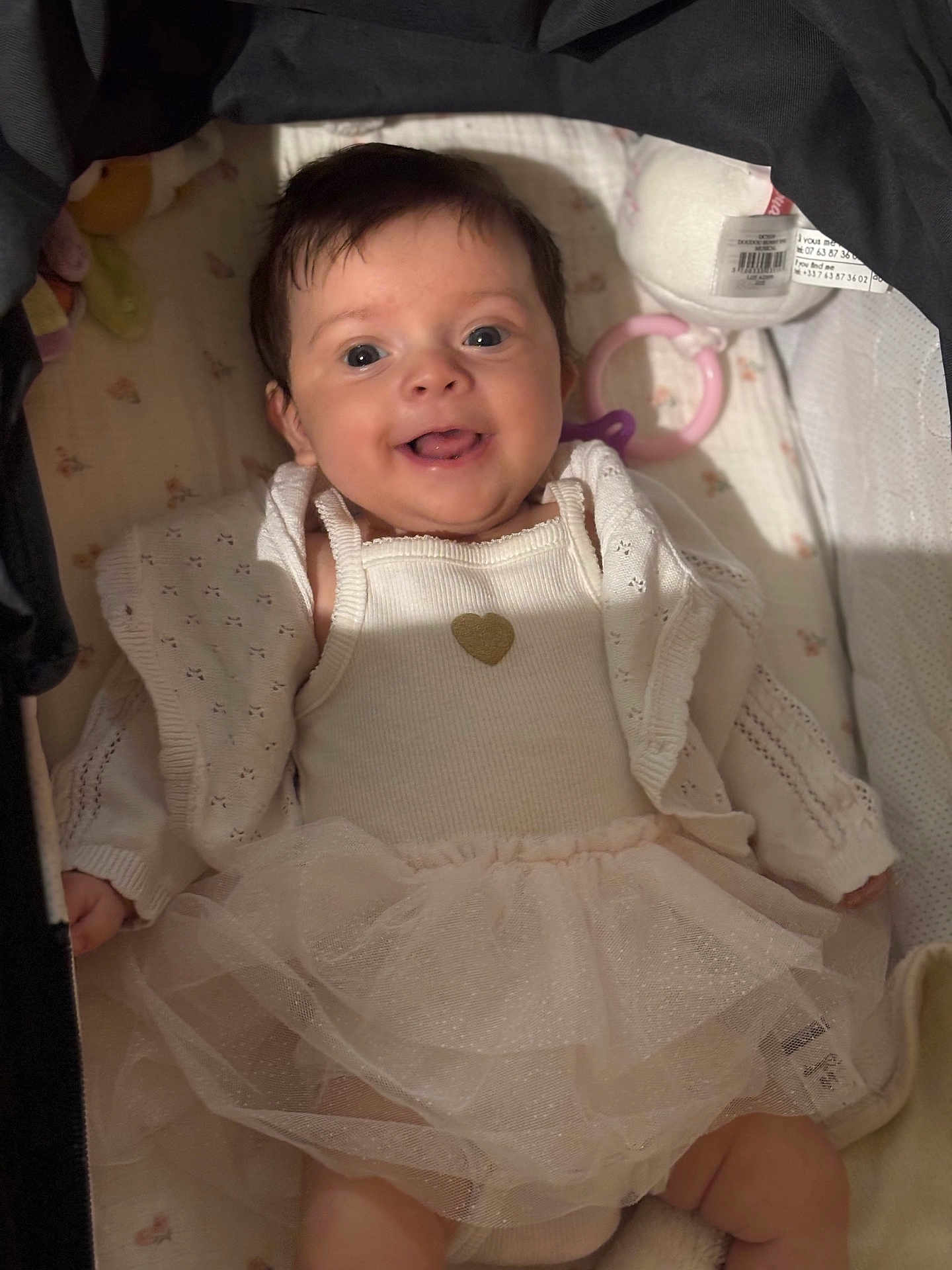 Louise participe au concours pour gagner de l'argent avec cette photo : baby, smiling, infant, tutu, white_clothing, crib, blanket, toy, cute, happy, face, child, indoors, soft_lighting, portrait, newborn, cozy, person, infant_fashion, sleeping_area